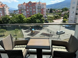 Un balcon doté de meubles en osier, donnant sur un parking et des immeubles d’habitation.