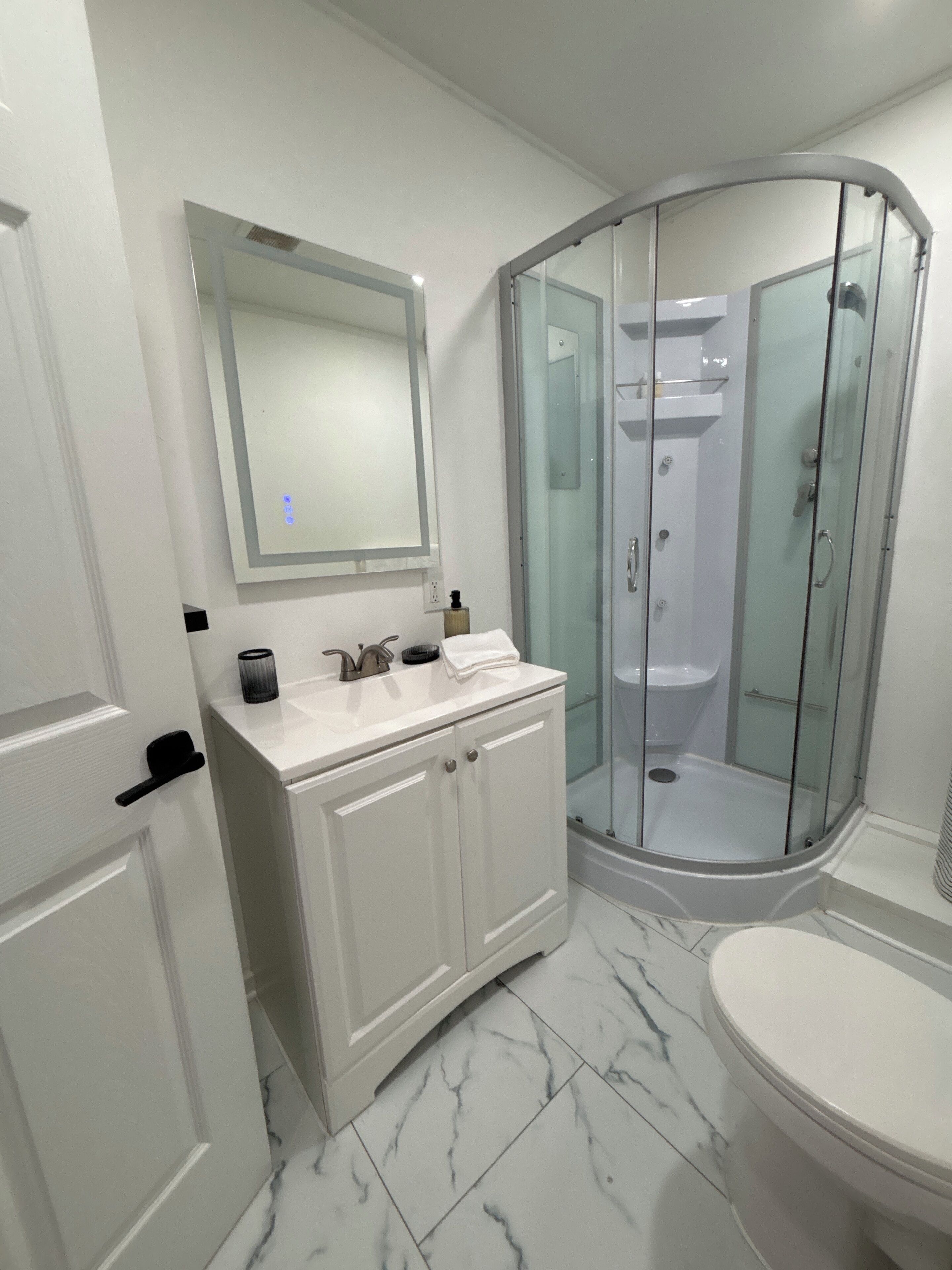 A modern bathroom with a white vanity, a glass-enclosed shower, and a marble floor.