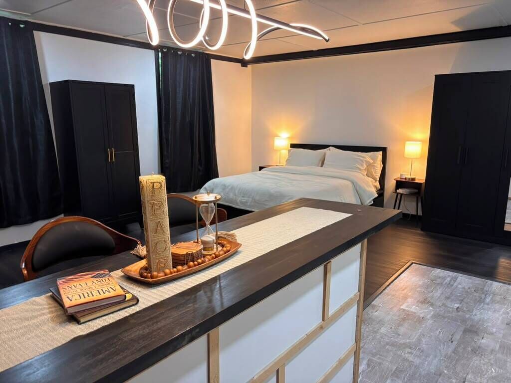 A hotel room with a bed, bedside lamps, a desk with a chair, and a large window.
