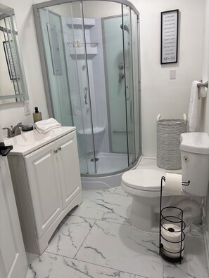 A modern bathroom with a glass-enclosed shower, a toilet, and a sink with a marble floor.