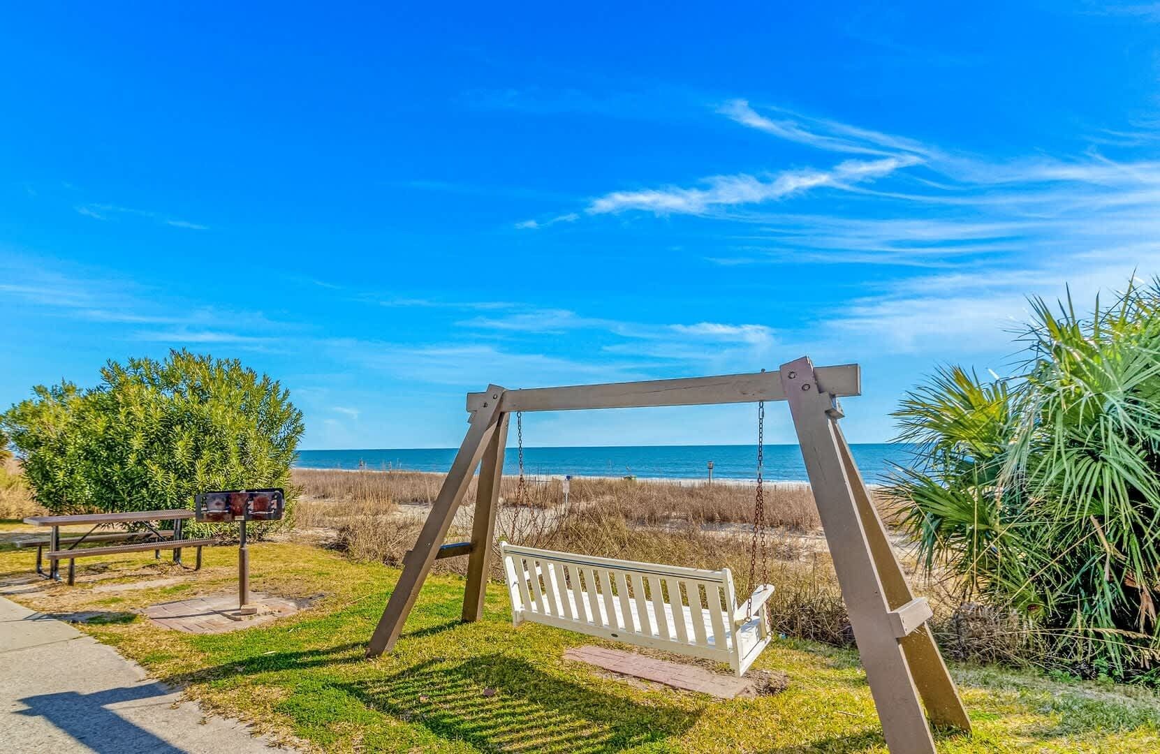 A swing set, picnic table, and bench near a beach.