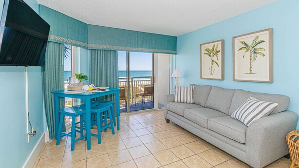 A room with a sofa, a dining table with chairs, a television, and two framed pictures on the wall. - Atlantica 200 Oceanfront Condo (Myrtle Beach)