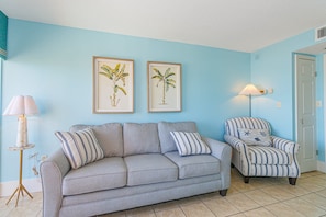 A living room with a grey sofa, striped armchair, two framed botanical prints, a floor lamp, and a small side table. - Oceanfront 1BR Retreat for 4! Atlantica 200 (Myrtle Beach)