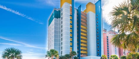 A multi-story hotel with a modern design, featuring balconies and a beach view.
