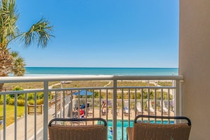 Ein Balkon mit Korbstühlen, einem Pool und Blick auf Strand und Meer.