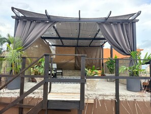 A covered outdoor seating area with a pergola structure, a small table, and chairs. - Modern 1BR Getaway near Beaches, Airport, and popular entertainment spots. (Montego Bay)