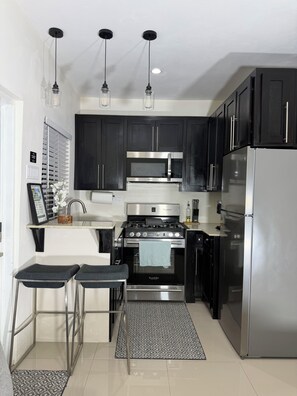 A modern kitchen with dark cabinets, stainless steel appliances, and pendant lighting. - Modern 1BR Getaway near Beaches, Airport, and popular entertainment spots. (Montego Bay)