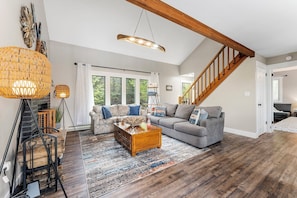 Ein geräumiges Wohnzimmer mit Couchtisch aus Holz, zwei Sofas, einem großen Teppich und einer Treppe mit Holzwangen.