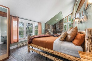 Un dormitorio amplio con una cama grande, una chimenea de piedra y vistas al exterior a través de amplias ventanas.