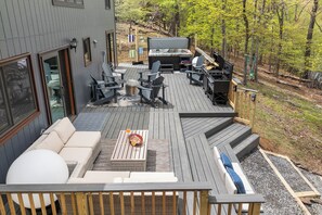 Una terraza con mobiliario exterior, una parrilla y vistas del bosque circundante.