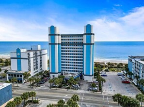Ein Hotel mit einem zentralen Turm, einem Parkplatz und Blick auf den Strand.