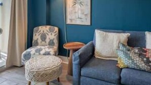 Et værelse med blå væg, en møbelstol med mønster, en sofa med puder, et lille rundt bord og en hængende lampe.