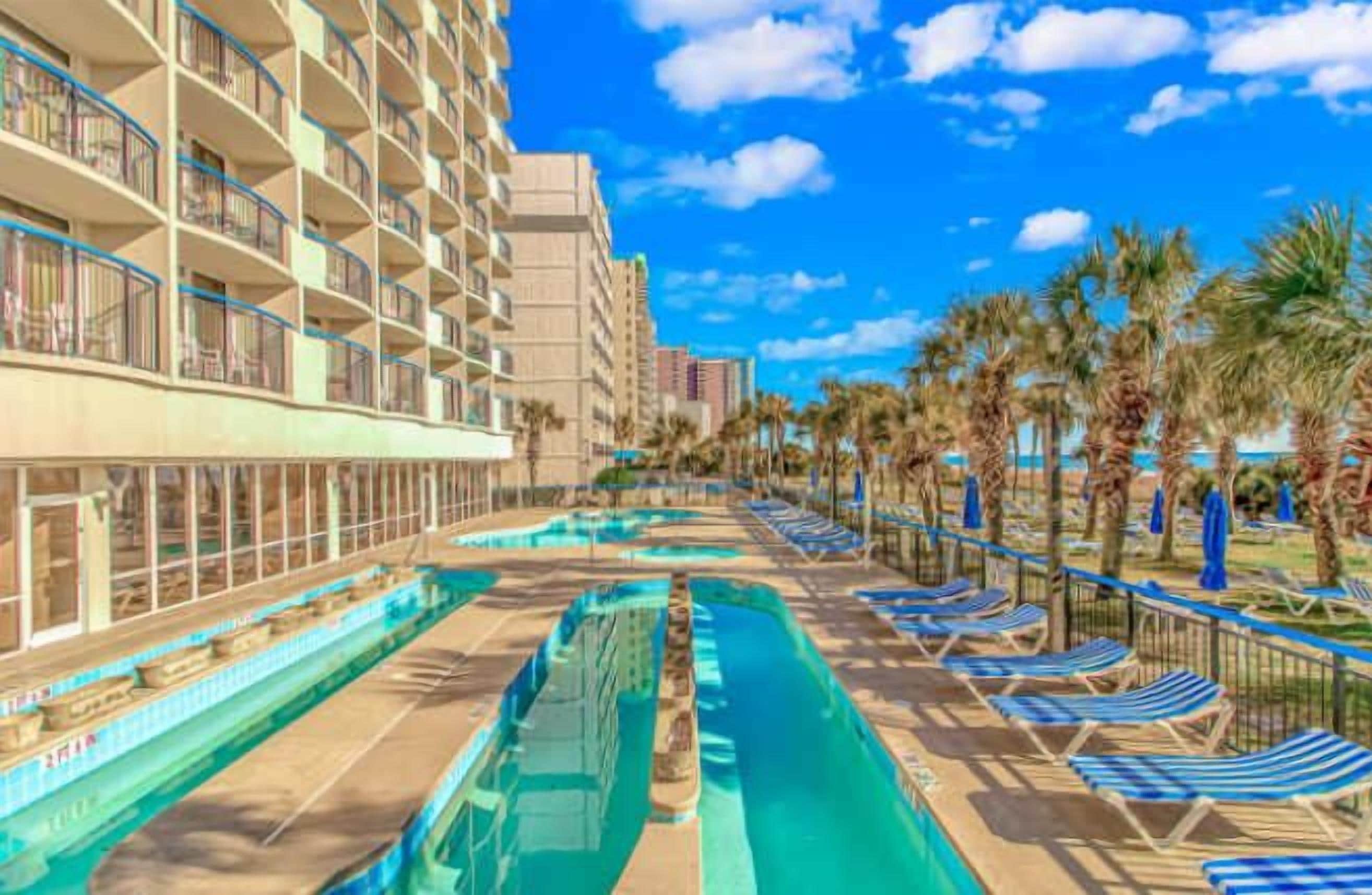 Un hotel con piscina, lettini e palme.