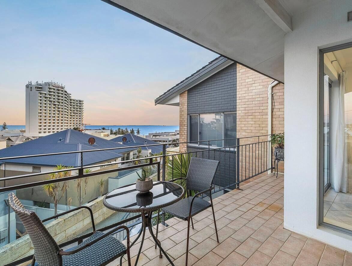 A balcony with a table and chairs, overlooking a cityscape and a body of water.