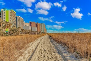 A sandy path leading to a beachfront with high-rise buildings in the background. - Boardwalk 440 Studio (Myrtle Beach)