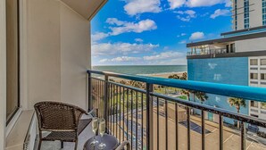 A balcony with a view of the ocean, a wicker chair, and a table with two glasses. - Boardwalk 440 Studio (Myrtle Beach)