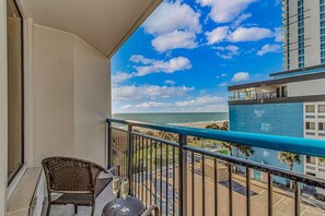 Ein Balkon mit Blick auf das Meer, ein Korbstuhl und ein Tisch mit zwei Gläsern.