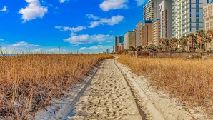 A sandy path leading to a beachfront with high-rise buildings in the background. - Boardwalk 440 Studio (Myrtle Beach)