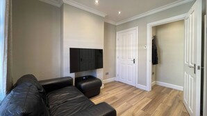 A living room with a black leather sofa, a flat-screen TV mounted on the wall, wooden flooring, and white doors. - Full House - Croydon Centre (Croydon)