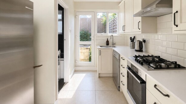 A modern kitchen with white cabinetry, a stainless steel refrigerator, a gas stove, and a window overlooking a garden. - Full House - Croydon Centre (Croydon)