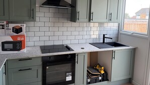 A kitchen with light green cabinets, a black range hood, a built-in oven, a sink, and a window. - Ivy Veil
A home away from home (Witham)