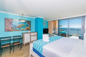 Une chambre d’hôtel avec un grand lit, un bureau, une chaise, une télévision et un balcon avec vue sur l’océan.
