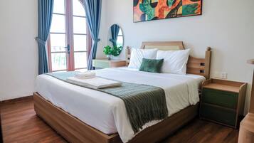A neatly made bed with a green throw blanket, a bedside table with a lamp, and a wall-mounted abstract painting.