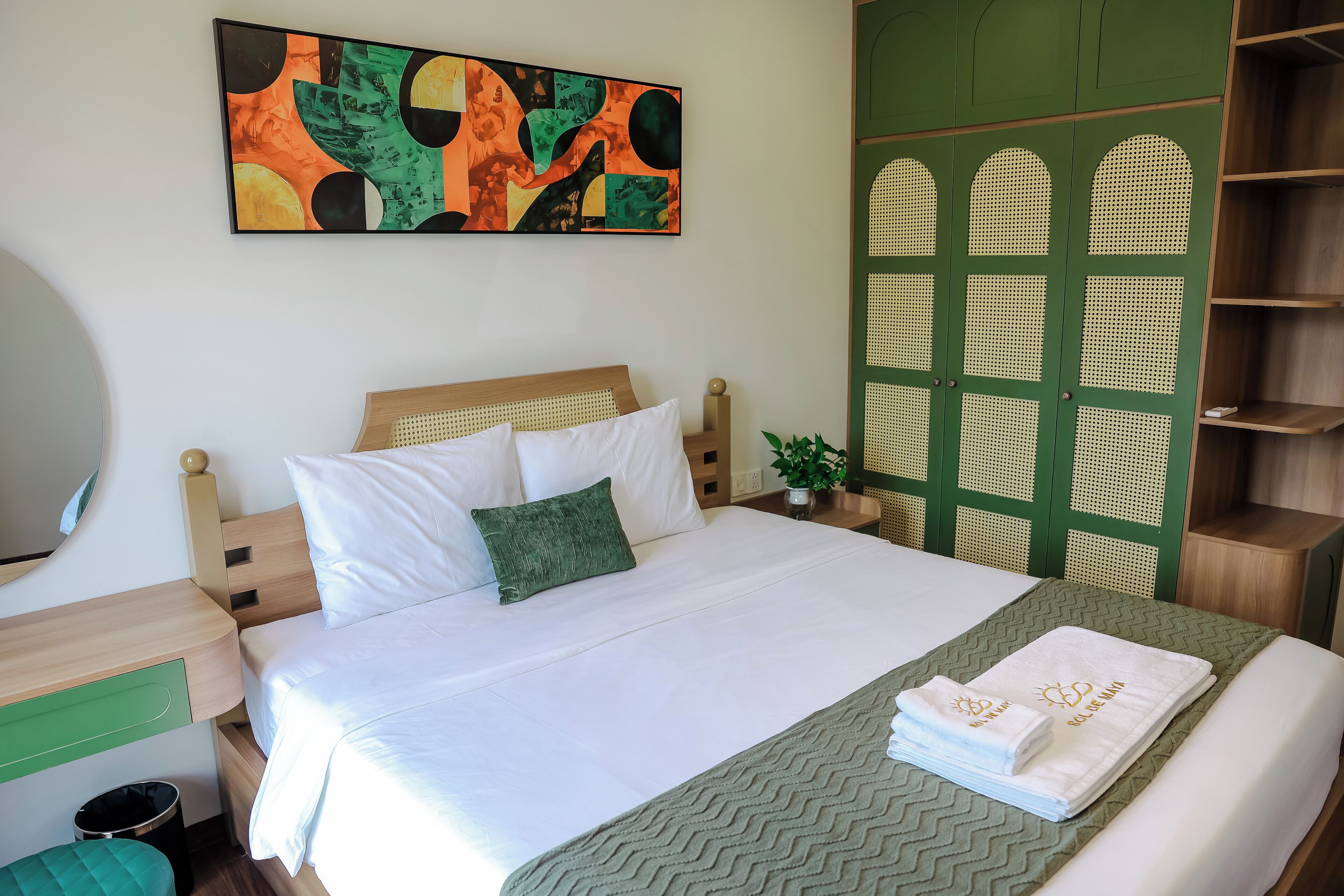 Un lit bien fait, avec du linge de lit blanc et un oreiller vert, un plaid à motifs verts et un ensemble de serviettes blanches ornées de lettres dorées, le tout posé sur un chemin de lit vert à motifs chevrons.
