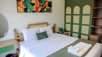 Un lit bien fait, avec du linge de lit blanc et un oreiller vert, un plaid à motifs verts et un ensemble de serviettes blanches ornées de lettres dorées, le tout posé sur un chemin de lit vert à motifs chevrons.