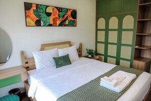 A neatly made bed with white linens and a green pillow, a green patterned throw, and a set of white towels with gold lettering on a green herringbone-patterned bed runner. - Cenlina Hotel & Apartment  (Phu Quoc)