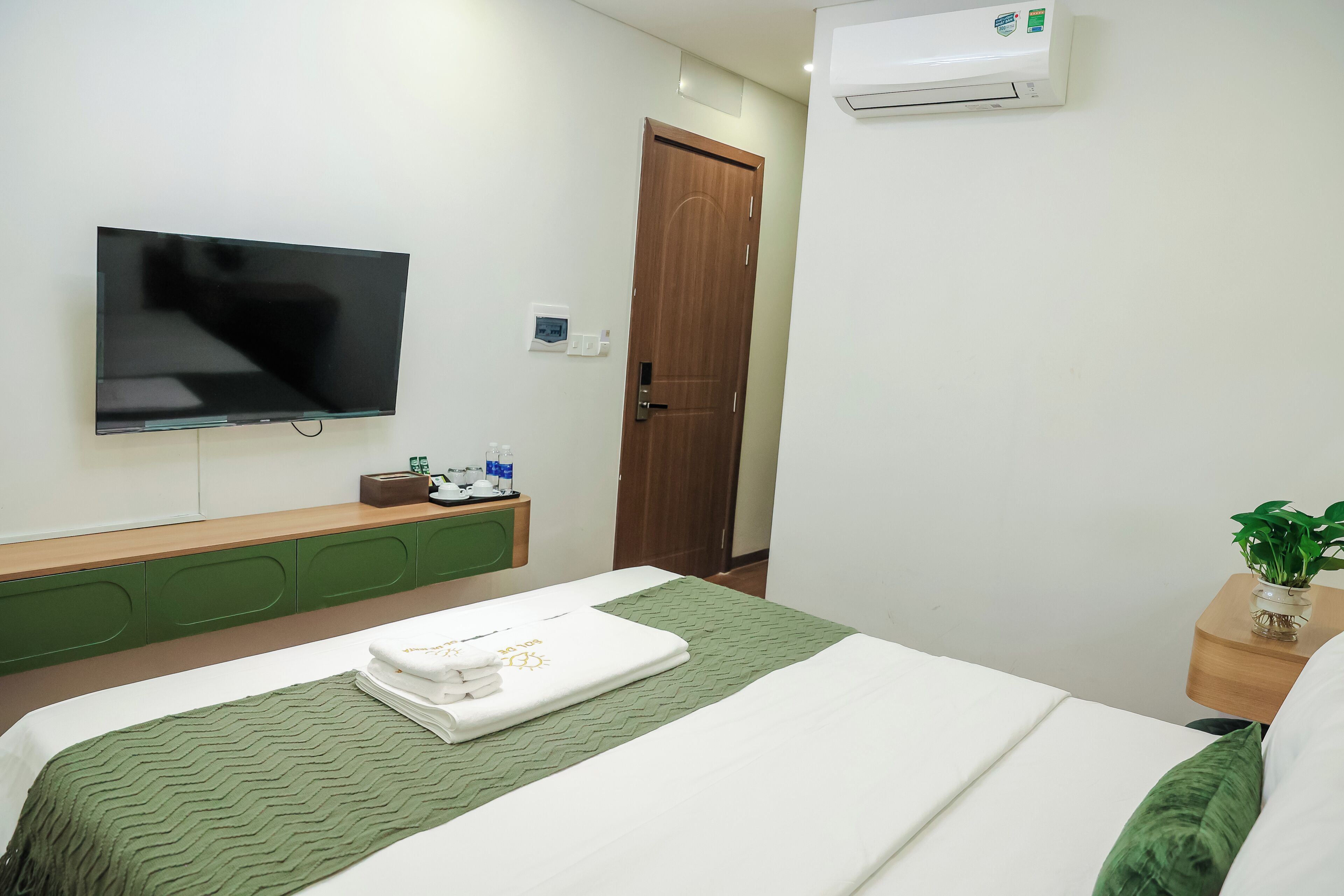 A hotel room with a bed, a television, a wooden door, and an air conditioning unit.