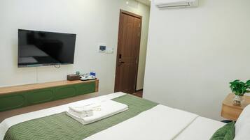 A hotel room with a bed, a television, a wooden door, and an air conditioning unit.