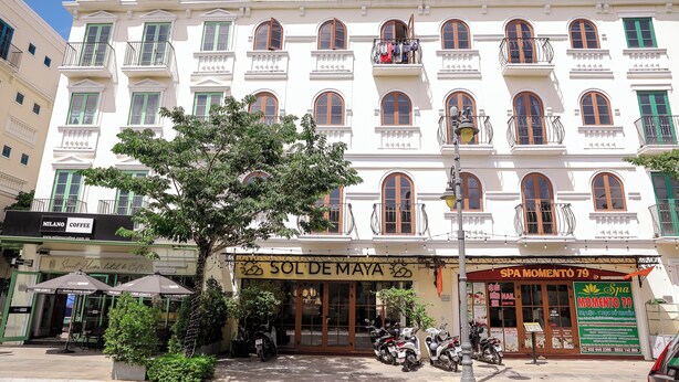 Un edifici d'alguns pisos amb una filera de balcons, una botiga amb un cartell i unes motores aparcades.