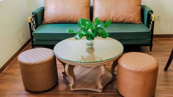 A green sofa with two brown cushions, a glass table with a plant, and two brown ottomans.
