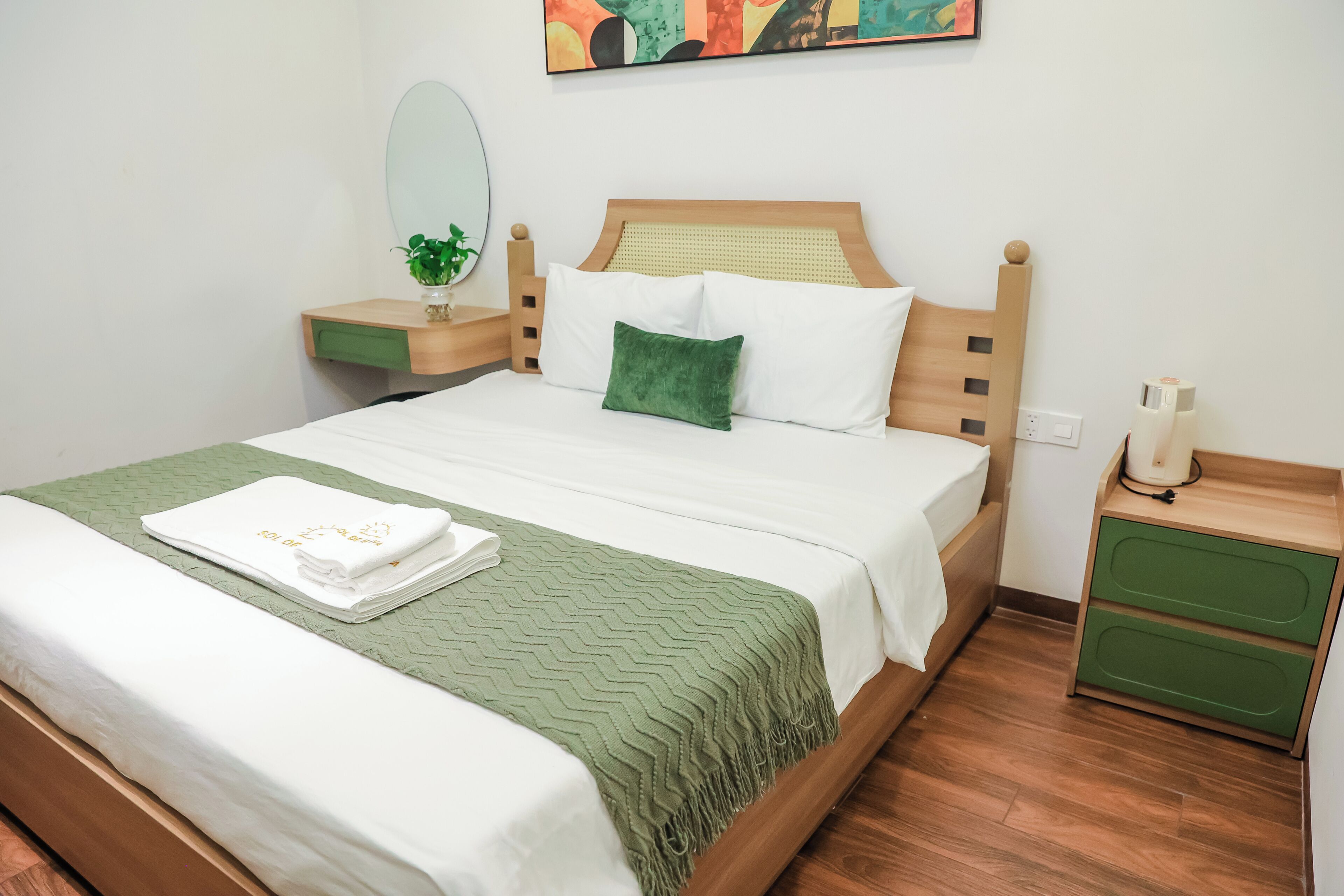 Een net opgemaakt bed met een groene deken, een wit kussen en een groen sierkussen op een houten hoofdbord.