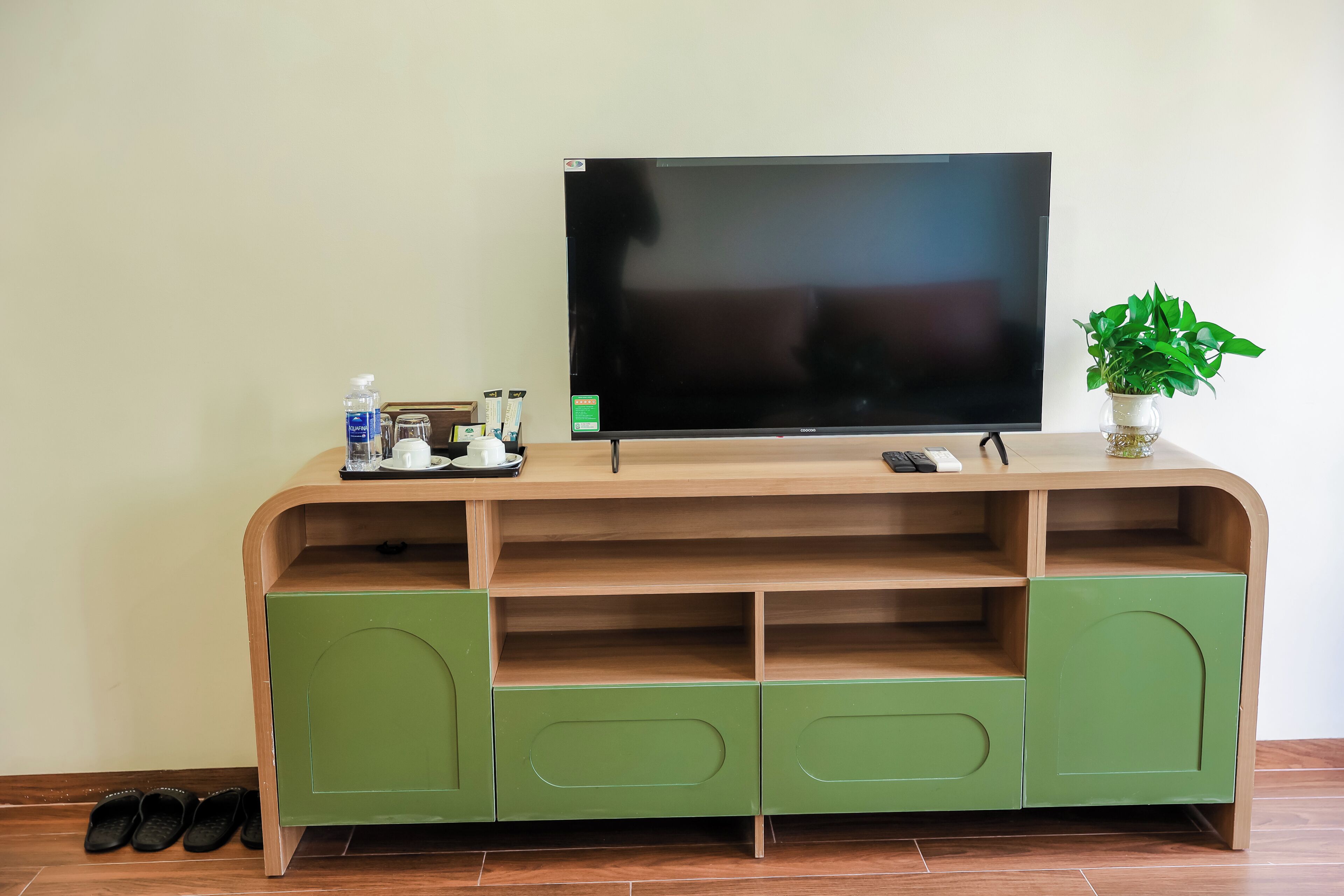 A flat-screen TV on a wooden entertainment unit with green cabinets and a plant on top.