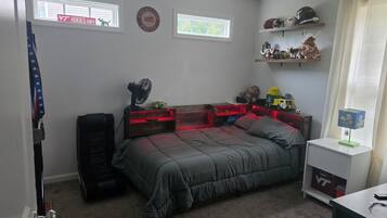A bedroom with a bed, a fan, a shelf with helmets, and a window with a sign.
