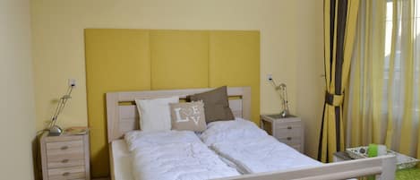 A bedroom with a bed, bedside tables, a TV, and curtains.