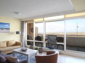 A living room with a large window, a sofa, a coffee table, and a TV. - Albatros by Interhome (Noordwijk)