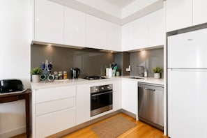 A modern kitchen with white cabinets, a stainless steel dishwasher, and a built-in oven.