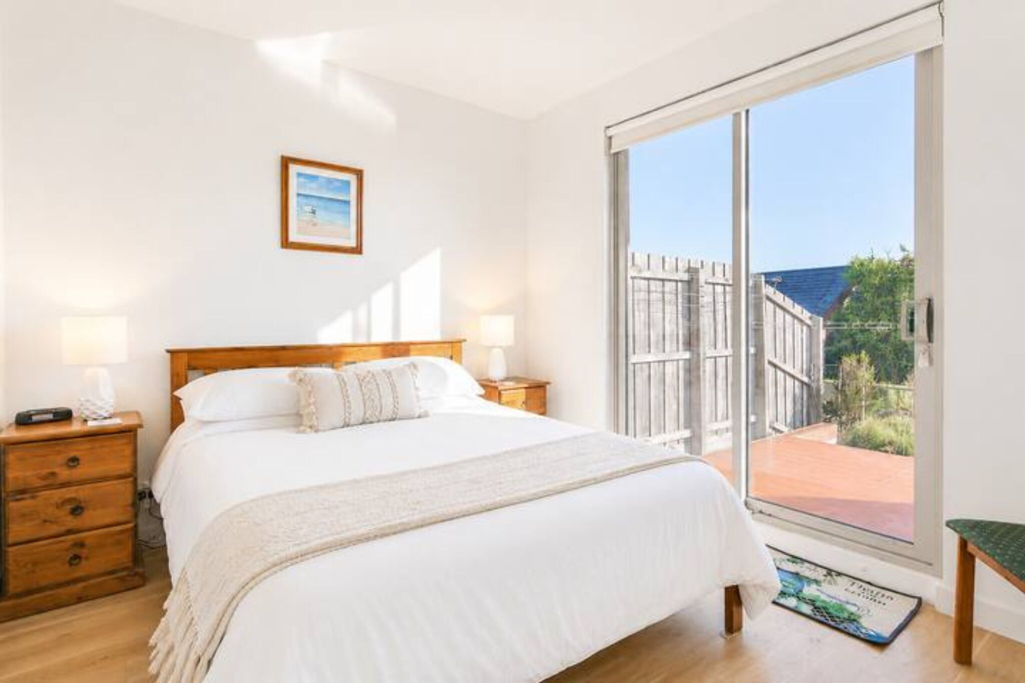 A bedroom with a bed, bedside tables, a nightstand, a window with a view of the outdoors, and a framed picture on the wall.