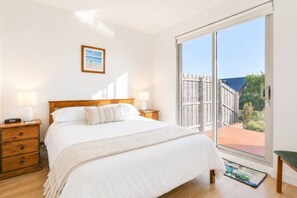 Een slaapkamer met een bed, nachtkastjes, een raam met uitzicht en een ingelijst foto aan de muur.