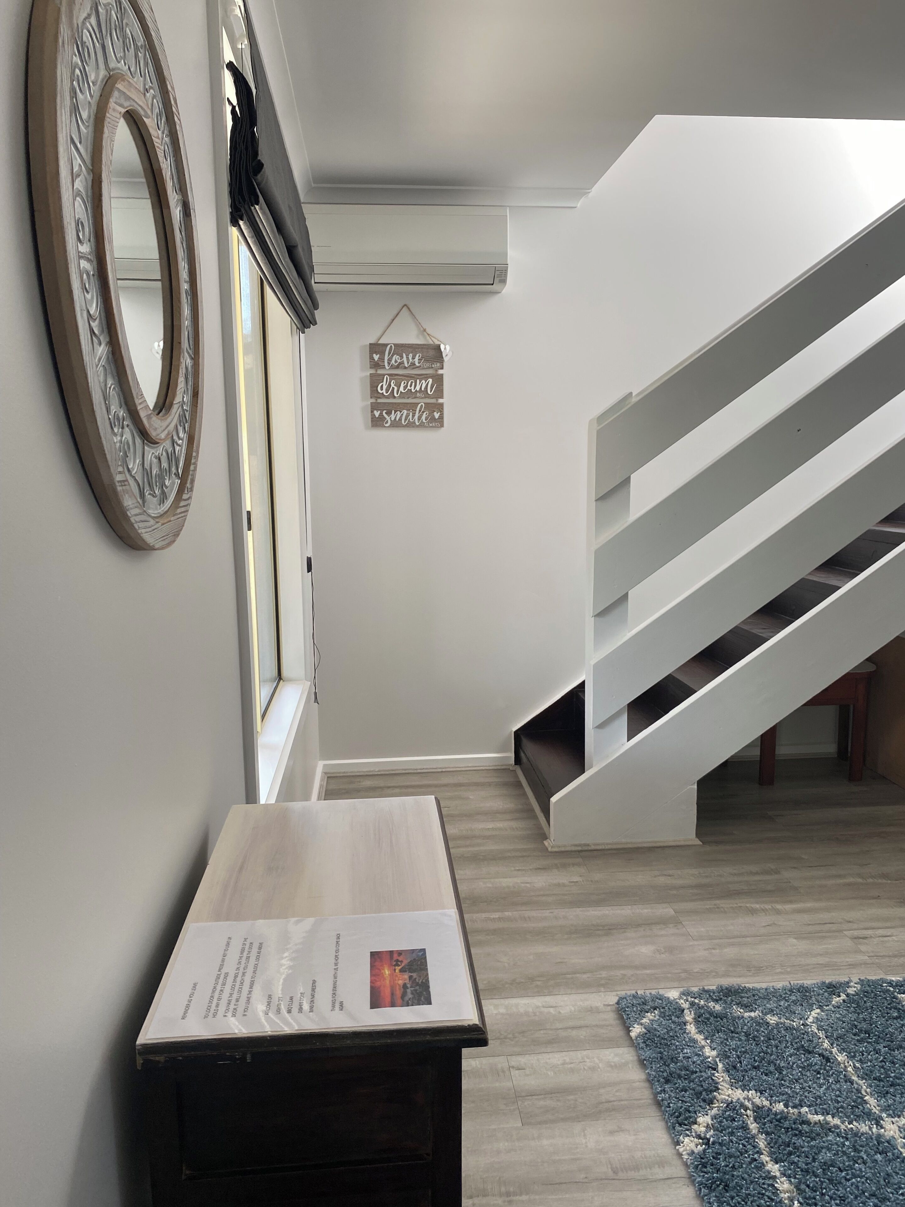 Un interior moderno con una escalera, una mesa de madera con un menú y un espejo decorativo.