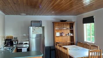 A kitchen with wooden ceiling, a dining table with chairs, and a refrigerator.