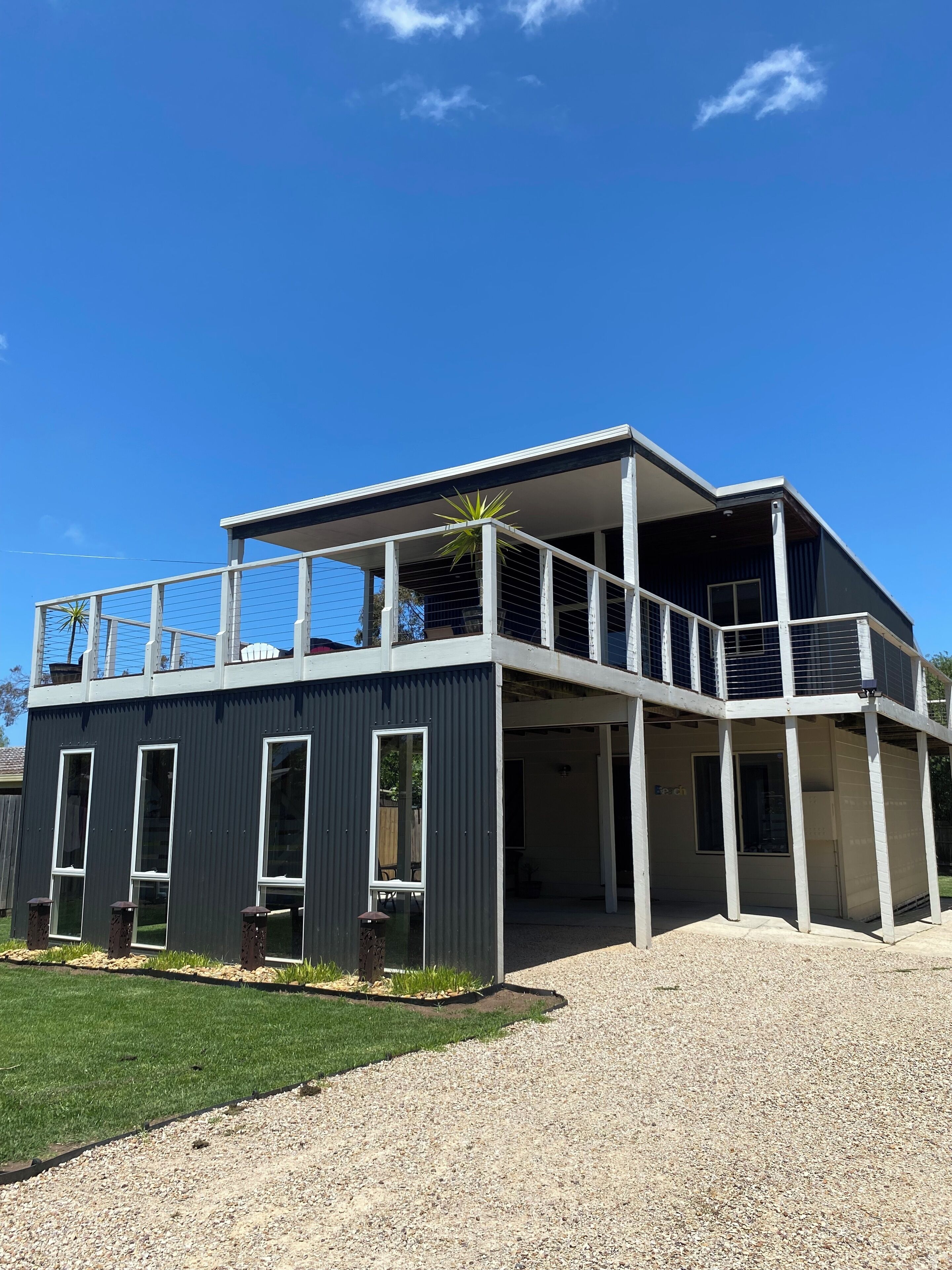 A modern two-story building with a balcony, large windows, and a gravel driveway.