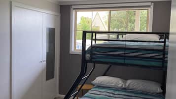 A bunk bed with striped bedding, a window with a view of greenery, and a white wardrobe.
