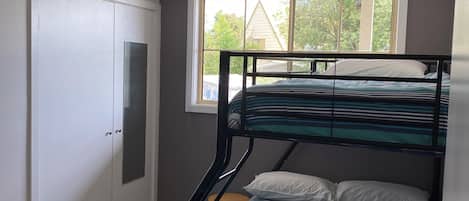 Un letto a castello con lenzuola a righe, una finestra vista su del verde e un'armadio bianco.