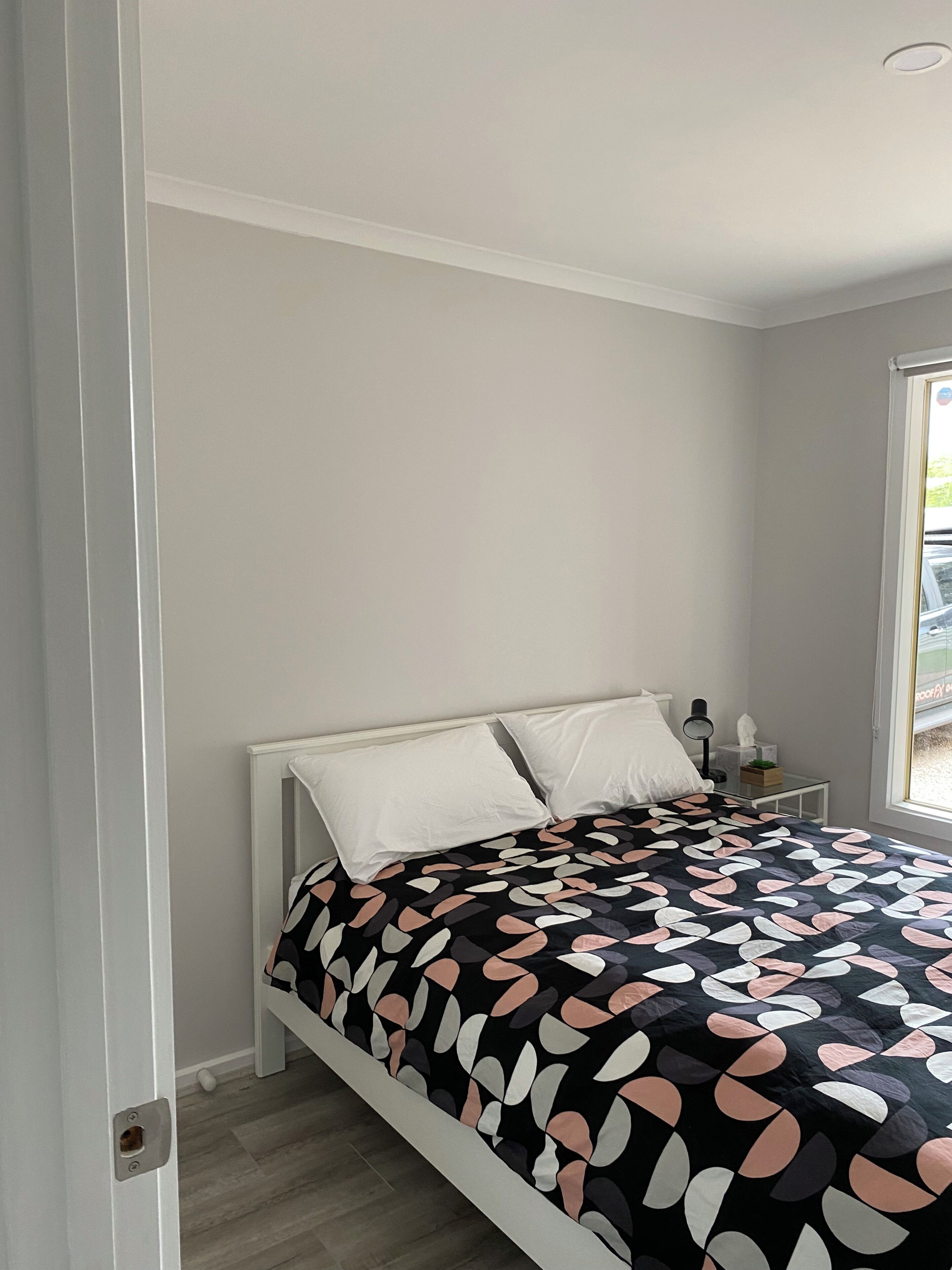 A bedroom with a bed, white walls, a window, and a nightstand with a lamp and tissues.