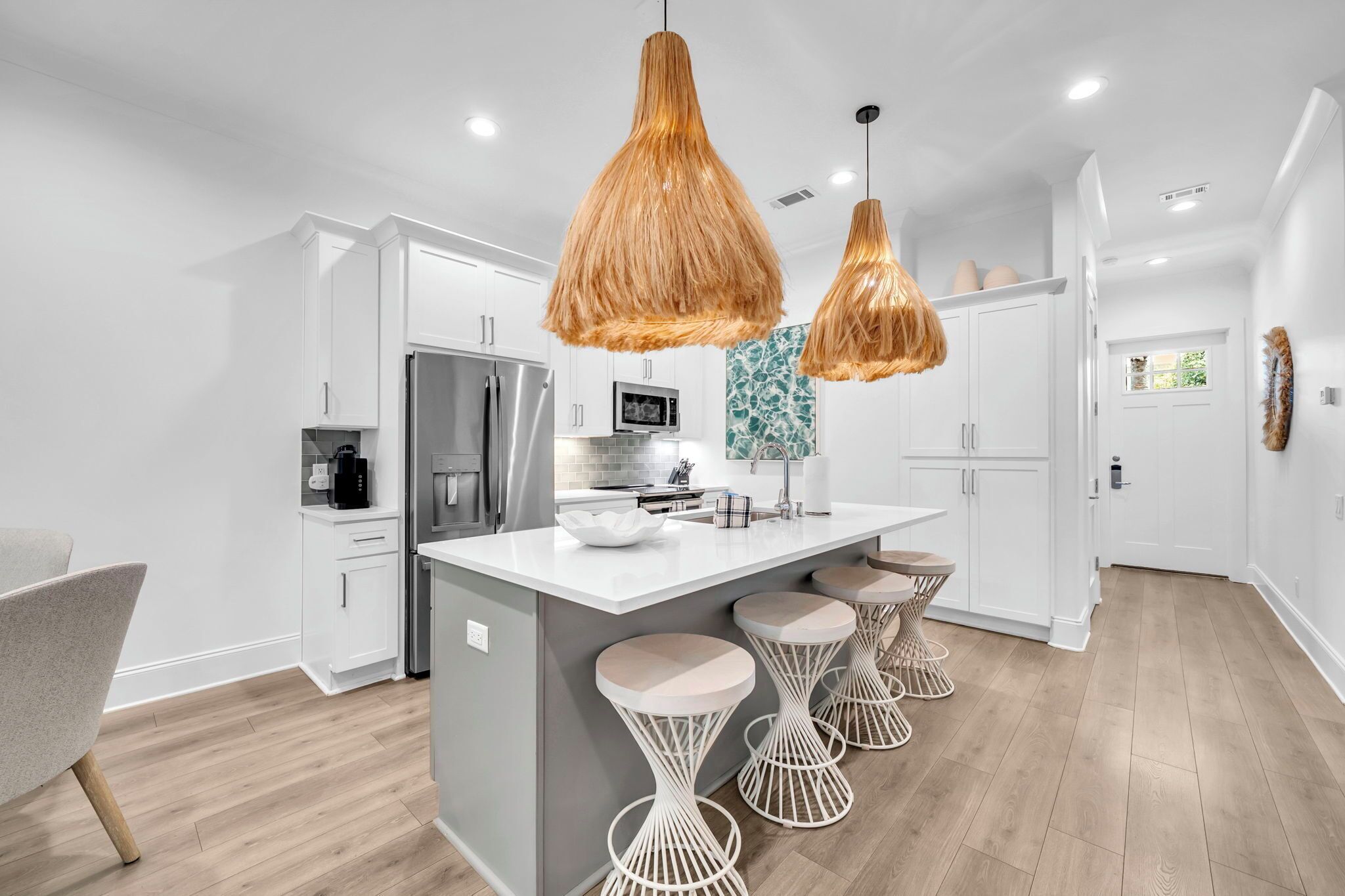 A modern kitchen with white cabinetry, a central island with stools, and hanging pendant lights.