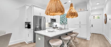 A modern kitchen with white cabinetry, a central island with stools, and hanging pendant lights.